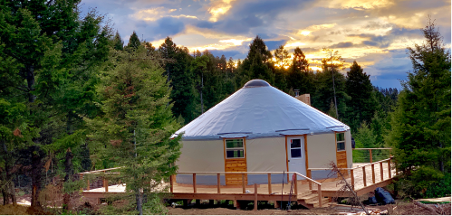 tan yurt with a grey roof on a large deck in the trees