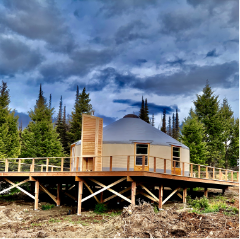 tan yurt with a grey roof on a large deck in the trees