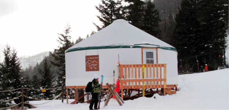 person with skis in front of a yurt ski lodge