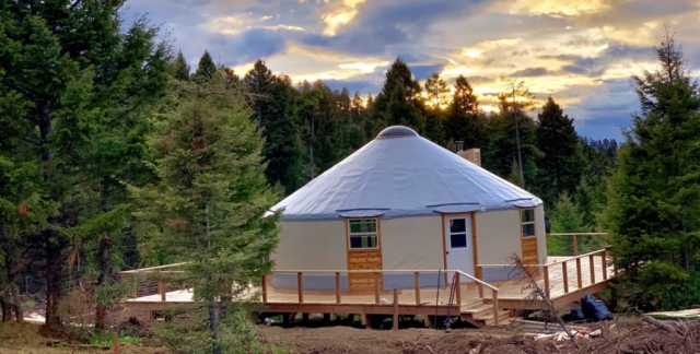tan yurt with a grey roof on a large deck in the trees