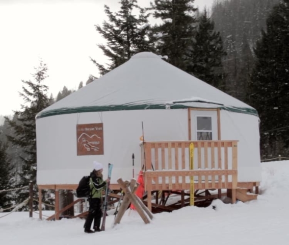 person with skis in front of a yurt ski lodge