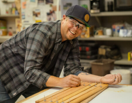 a man smiles while leaning over a table with wood on it