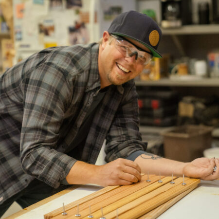 a man smiles while leaning over a table with wood on it
